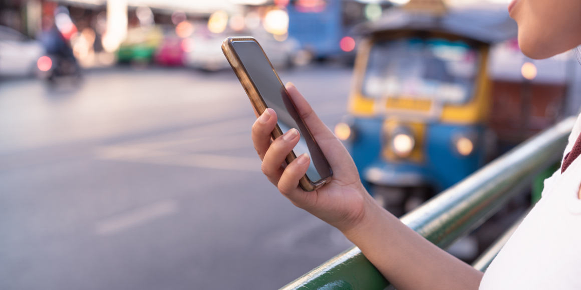 a person holding a smartphone in their right hand on a busy road